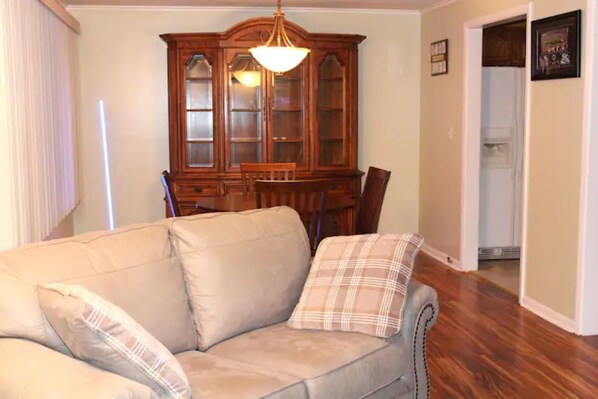 A living room with a beige sofa, two plaid pillows, a wooden cabinet, and a dining table. - Spacious apartment in Buffalo (Buffalo)