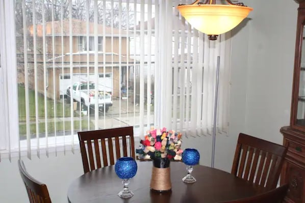 A dining area with a round table, two chairs, a vase with flowers, and a hanging light fixture.