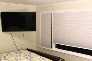 A bedroom with a bed, a television mounted on the wall, and a window with blinds. - Spacious apartment in Buffalo (Buffalo)