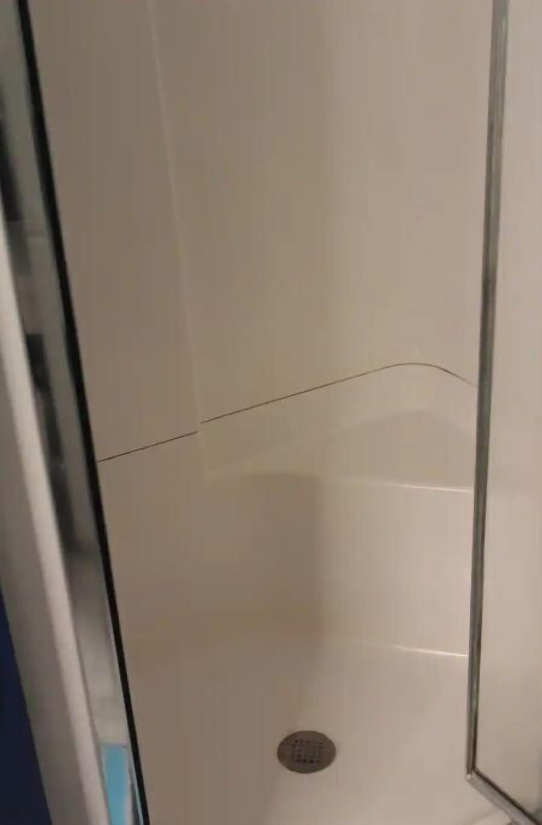 Un espacio de ducha estrecho y cerrado, con paredes de azulejos y un desagüe en la parte inferior.