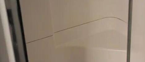 Un espacio de ducha estrecho y cerrado, con paredes de azulejos y un desagüe en la parte inferior.