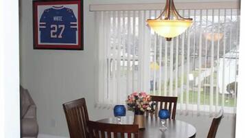 A dining area with a round table, chairs, a chandelier, a framed sports jersey, and a window with blinds.
