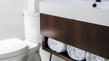 A modern bathroom with a white toilet, a white sink with a wooden vanity, a hanging plant, and a towel rack with towels.