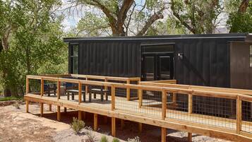A modern cabin with a wooden deck and a black exterior, surrounded by trees.