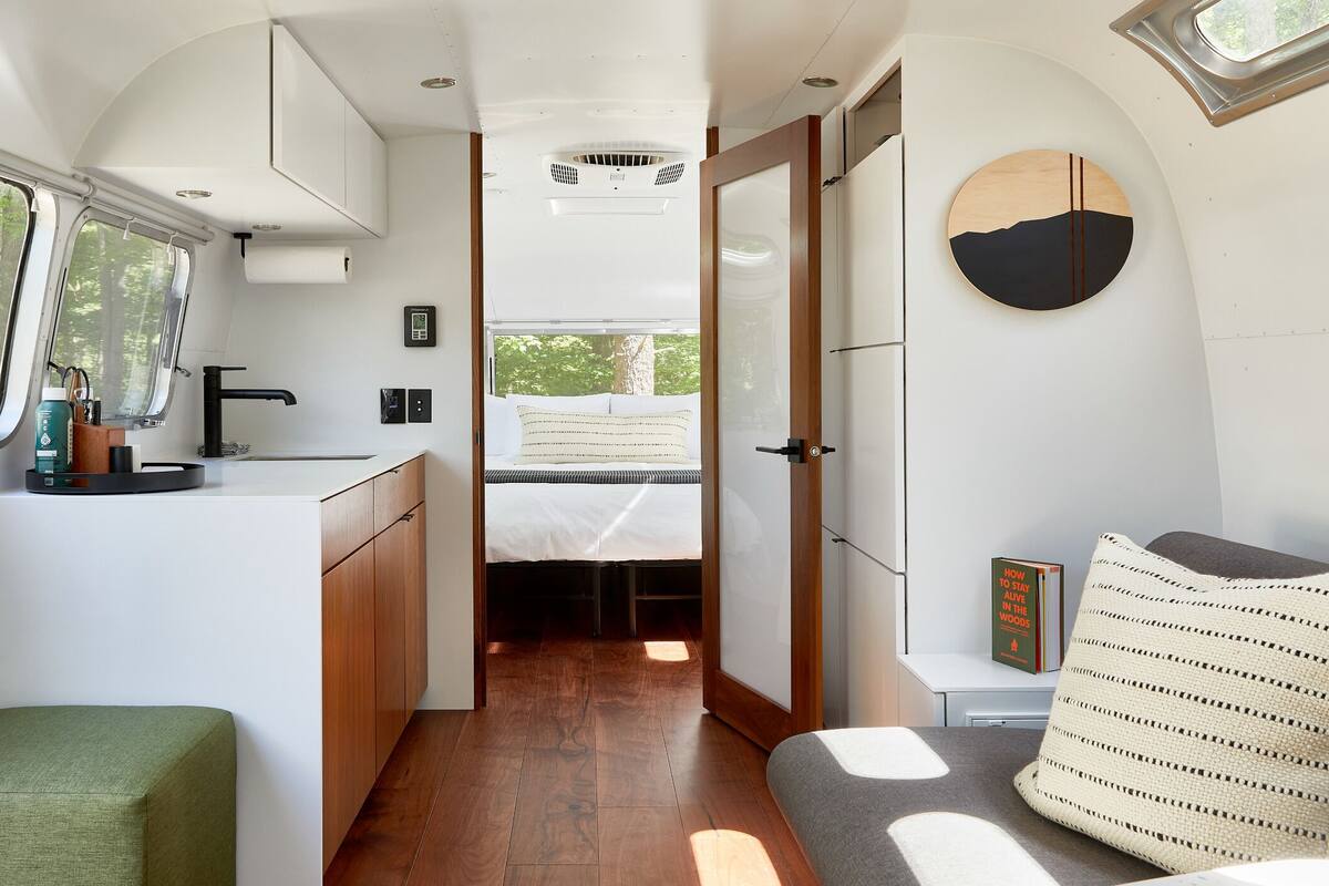 A compact RV interior with a kitchenette, a bed, and a seating area.