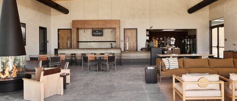 A spacious lounge area with a fireplace, seating arrangements, and a kitchen area in the background.