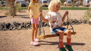 Two children on a swing in a park with a clear sky and distant mountains.