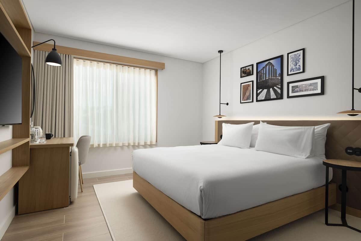 Ein modernes Hotelzimmer mit einem großen Bett, einem Schreibtisch, einem Sessel, einem Fernseher und Bildern an der Wand.