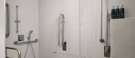 A modern bathroom with white tiled walls, a wooden floor, and multiple handrails.