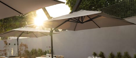 An outdoor dining area with round tables and chairs, large umbrellas, and a modern design.