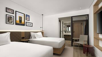 A hotel room with two beds, a TV, a desk, and a bathroom visible through an open door.