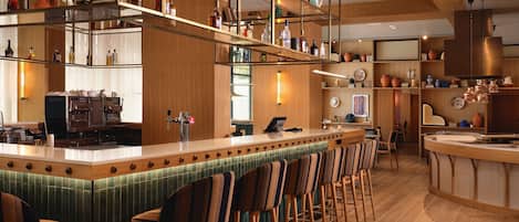Zona de bar con una barra alargada, varios taburetes y estantes llenos de botellas.