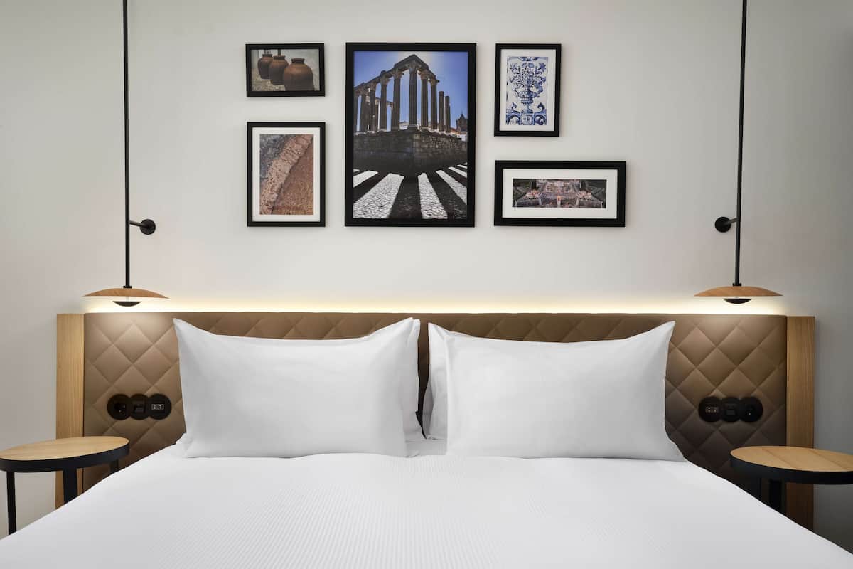Ein Hotelzimmer mit einem großen Bett, zwei Nachttischen, einem Kopfteil mit integrierter Beleuchtung und vier gerahmten Bildern an der Wand.