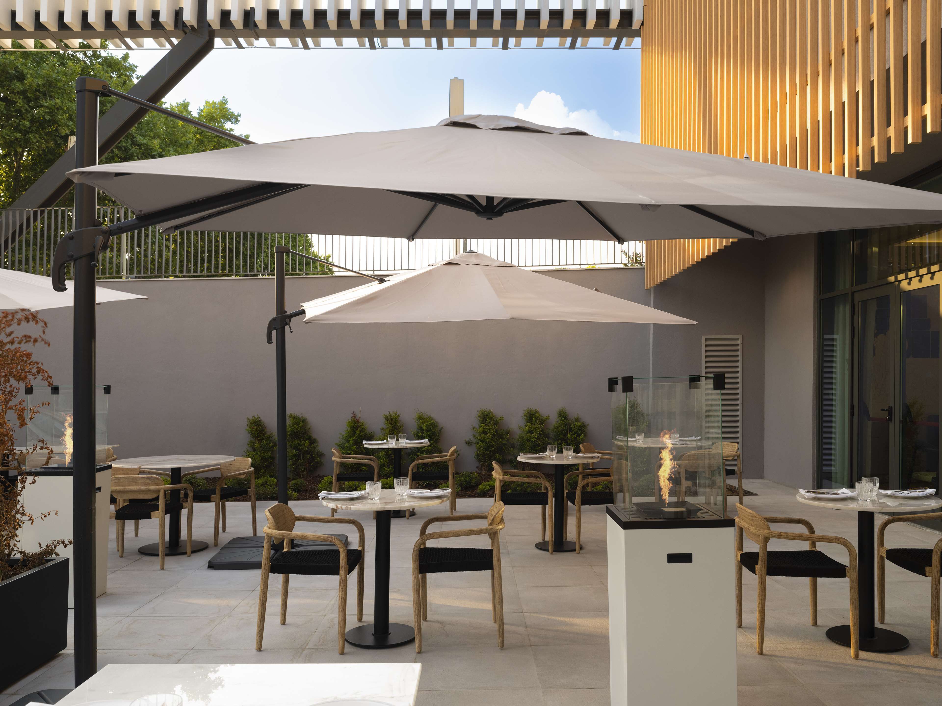 An outdoor patio area with round tables and chairs, covered by large umbrellas, and a glass display case with a fire feature.