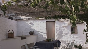Un espace extérieur aménagé dans un style rustique, avec une table, des chaises et un panier de fruits.