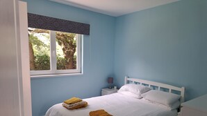 A bedroom with a bed, a nightstand, a window with a view of trees, and a door. -  Holiday home with lake and grounds for families and groups. (L'Auvergneuse, Fenery)