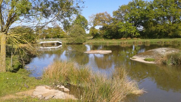 A calm river with a small bridge and surrounding greenery. -  Holiday home with lake and grounds for families and groups. (L'Auvergneuse, Fenery)