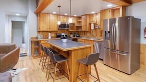Eine moderne Küche mit Holzschränken, einer zentralen Kochinsel mit Barhocker, einem Edelstahlkühlschrank und einer Mikrowelle.
