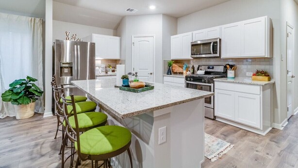 A modern kitchen with white cabinets, a stainless steel refrigerator, a microwave, and a large island with bar stools.