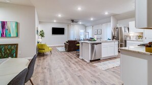 A modern kitchen with white cabinetry, a central island, and a dining area with a yellow chair.
