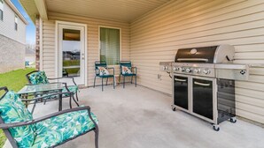 An outdoor patio with a grill, chairs, and a glass table.
