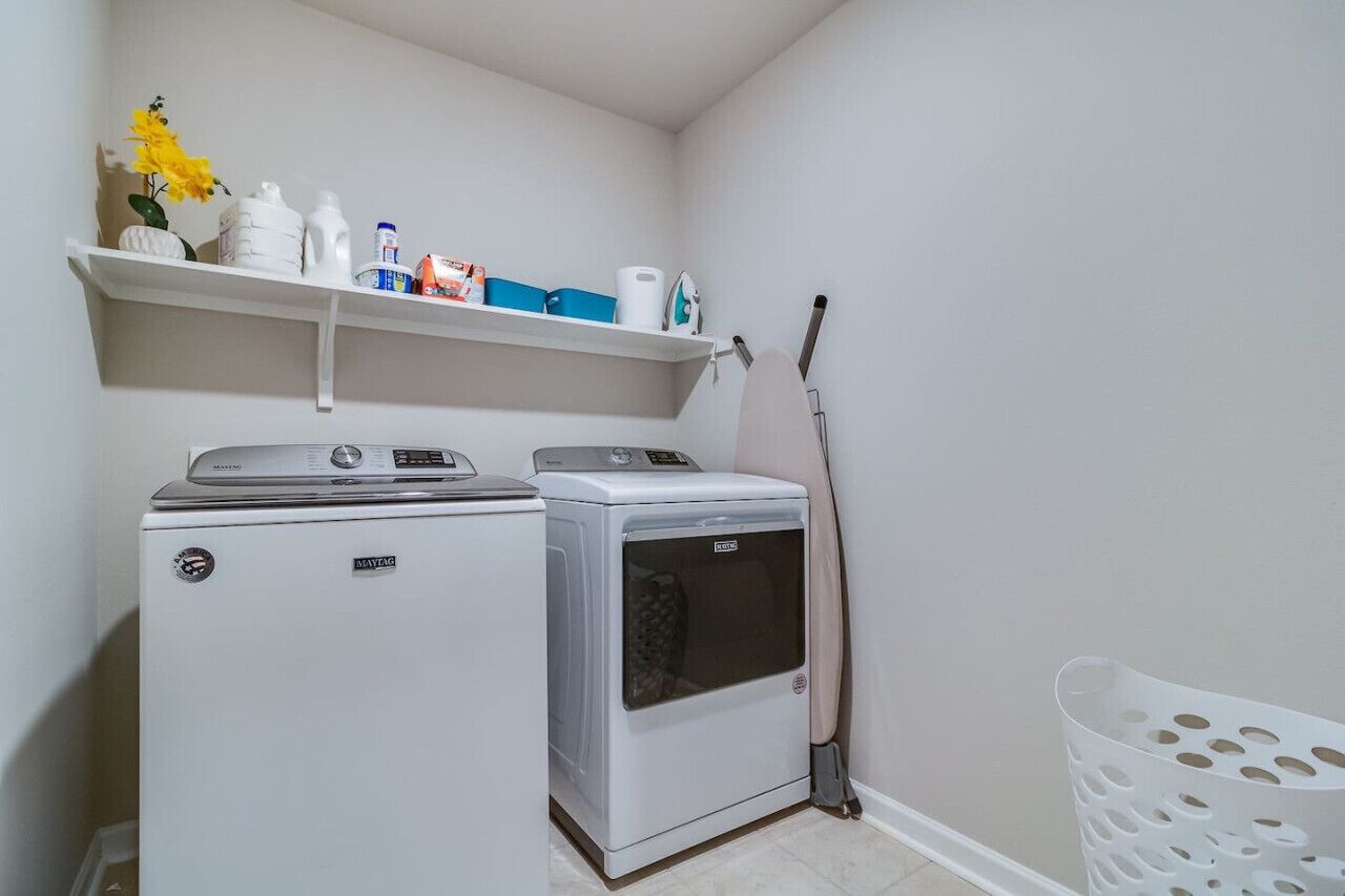 A laundry room with two washing machines, a shelf with cleaning supplies, and a mop leaning against the wall.