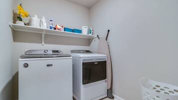 A laundry room with two washing machines, a shelf with cleaning supplies, and a mop leaning against the wall.