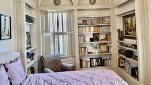 Un dormitorio con un ventanal grande, estanterías, una silla y una cama.