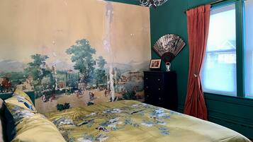 Een slaapkamer met een groot muurschildering, een bed met bloemenbedekte lakens, een dressoir en een raam met gordijnen.
