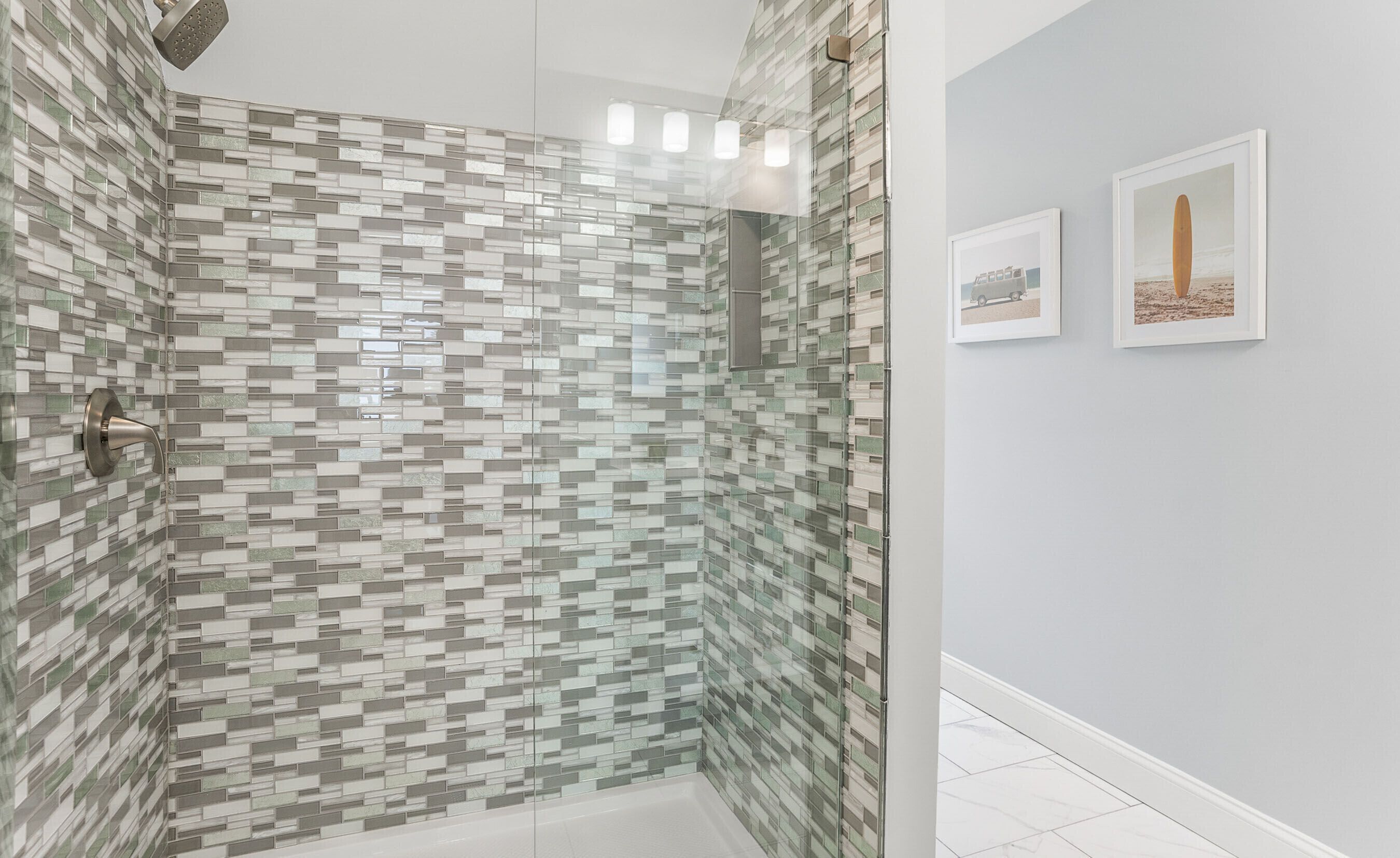 Une douche avec un mur recouvert de mosaïques, un tableau encadré au mur et un sol carrelé.