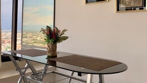 En modern lägenhet med ett matbord i glas, utsikt över staden och två inramade konstverk på väggen.