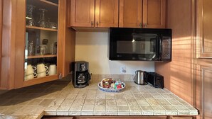 A kitchen with wooden cabinets, a microwave, a coffee maker, and a bowl of snacks. - Step into history & unwind at Elixir apt a charming 🏡 at the❤️of NYHudson Valley (Highland)