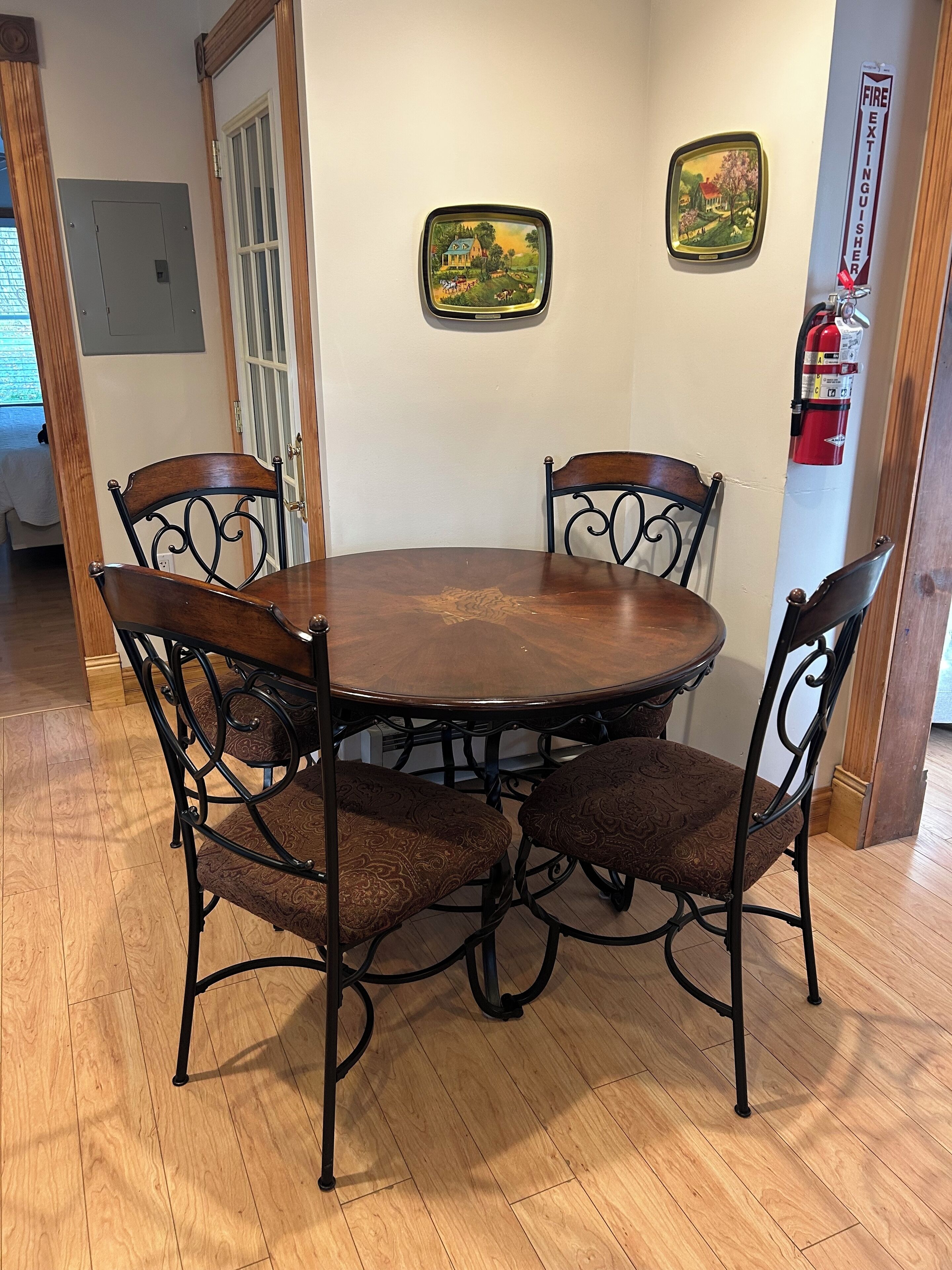 A dining area with a round wooden table and four ornate metal chairs with cushioned seats.