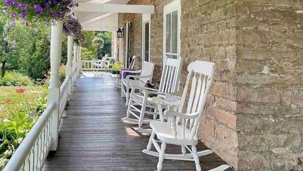 A wooden porch with white rocking chairs and a hanging flower basket. - Step into history & unwind at Elixir apt a charming 🏡 at the❤️of NYHudson Valley (Highland)