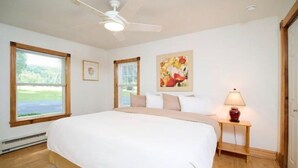 A bedroom with a large bed, a ceiling fan, two windows, a nightstand with a lamp, and a painting on the wall. - Step into history & unwind at Elixir apt a charming 🏡 at the❤️of NYHudson Valley (Highland)