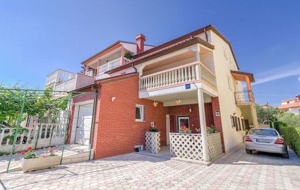 Une maison à deux étages avec un balcon, un garage et une voiture garée devant.