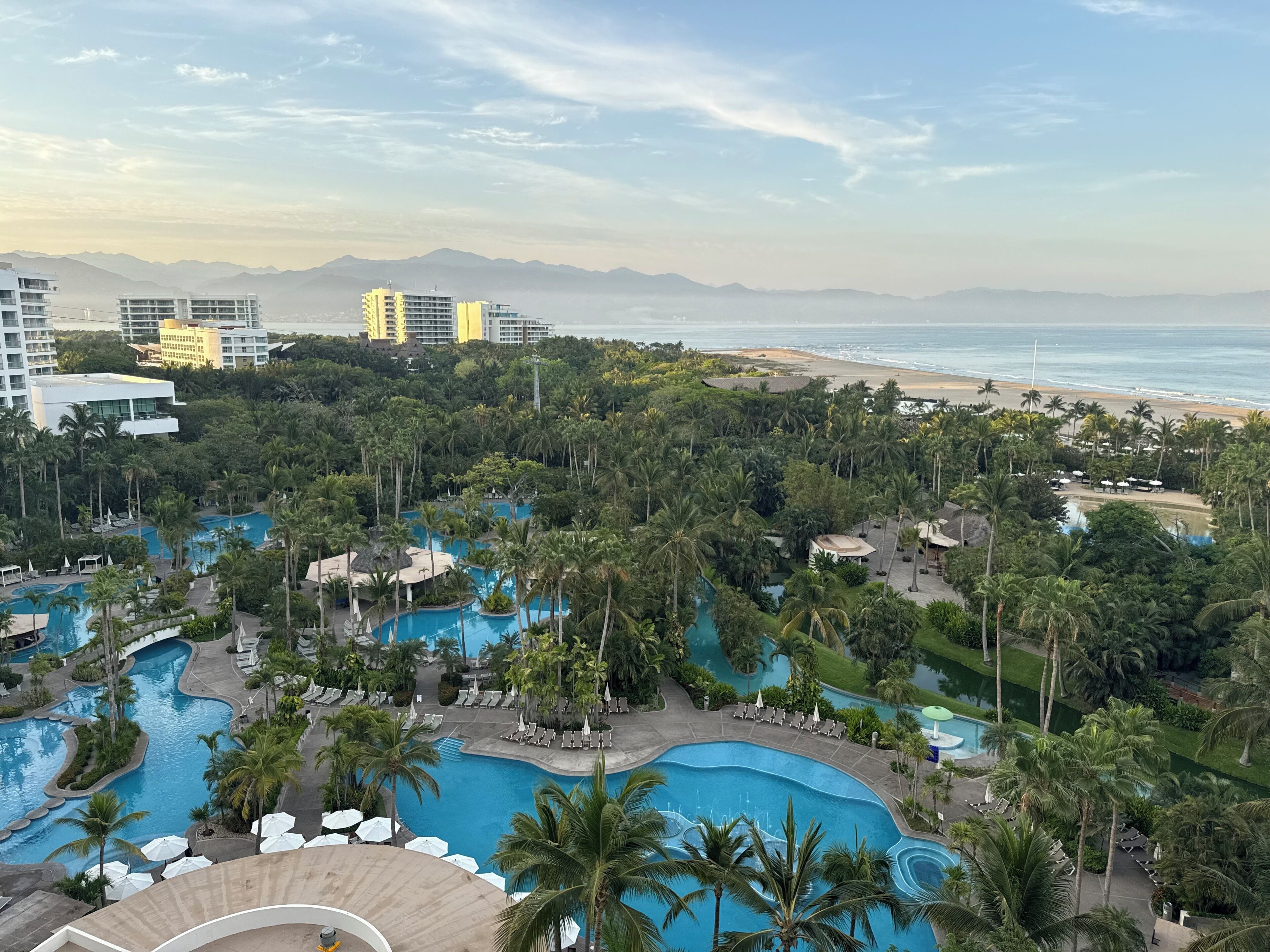 A resort with multiple swimming pools, palm trees, and a beach view.