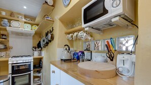 A kitchen with a stove, oven, microwave, and various utensils and dishes on shelves. - Charming Historical Cottage in Scarborough (Scarborough)