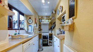 A narrow kitchen with white cabinets, a dishwasher, a stove, and various kitchen utensils. - Charming Historical Cottage in Scarborough (Scarborough)