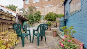 A patio with a table and chairs, surrounded by potted plants and a stone wall. - Charming Historical Cottage in Scarborough (Scarborough)