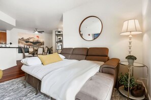 A modern bedroom with a bed, a round mirror, a bedside table with a lamp, and a small potted plant. - Idlewild Park condo by downtown + Pool & Parking (Reno)