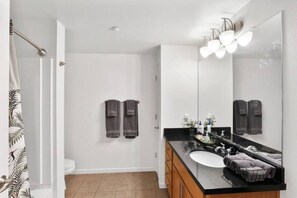 A modern bathroom with a black countertop, white sink, and a large mirror. There are two towels hanging on the wall and a shower curtain with a leaf pattern. - Idlewild Park condo by downtown + Pool & Parking (Reno)