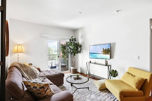A living room with a sofa, armchair, coffee table, and a TV mounted on the wall.