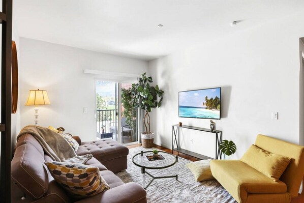 Una sala de estar con sofá, sillón, mesa de centro y televisor montado en la pared.