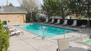 Una piscina con sillas de descanso y una mesa, rodeada por una valla y árboles.