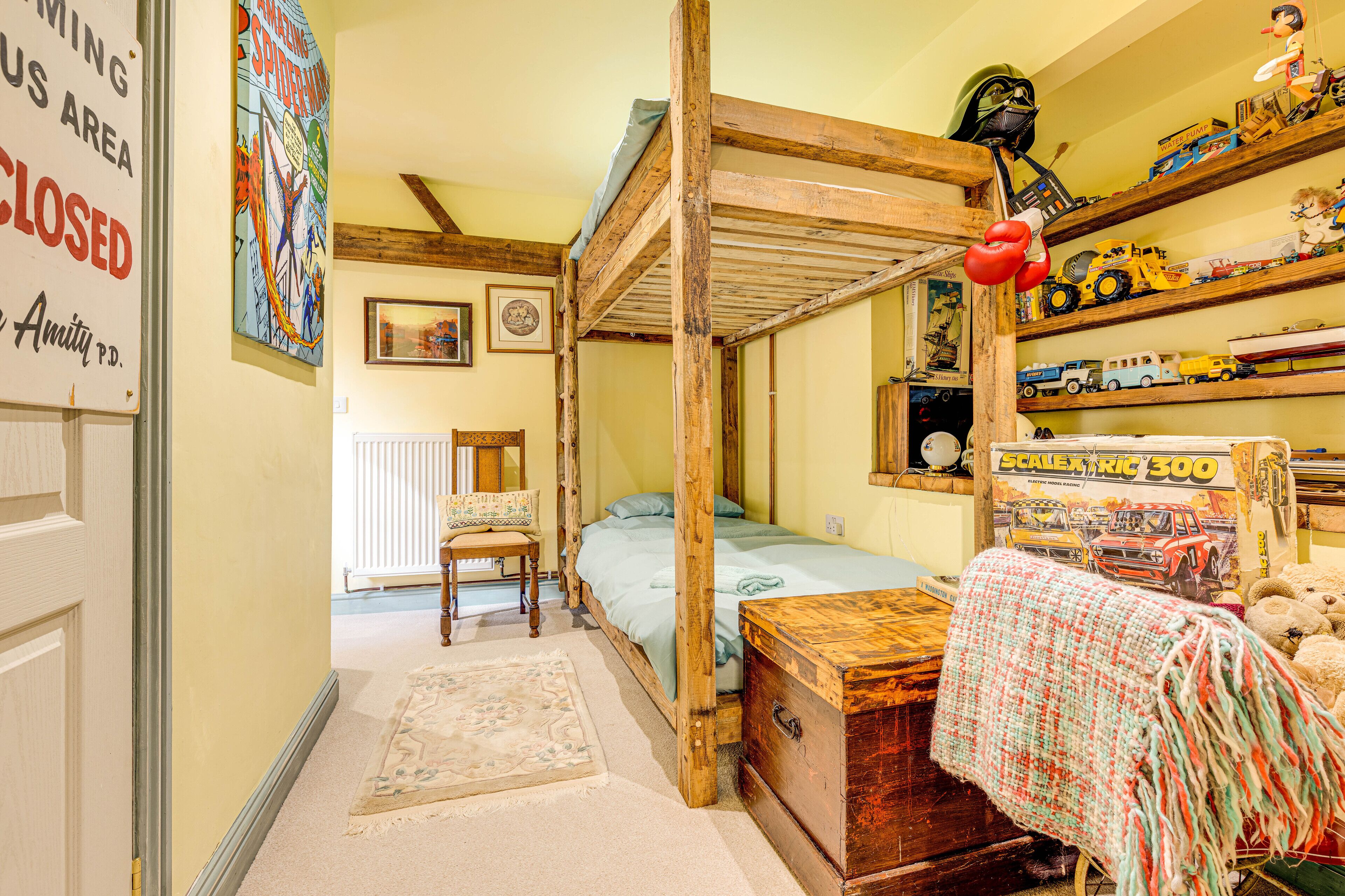 Une chambre à coucher avec un lit à baldaquin, une commode en bois, un radiateur et une étagère où sont exposées des voitures miniatures.
