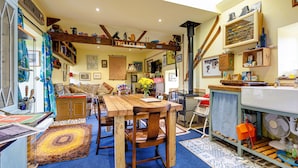 A cozy, well-lit room with a wooden table and chairs, a blue carpet, and a variety of decorations including a 'TROLLEY BUS' sign. - Family Country Cottage With a Private Valley View (Scarborough)