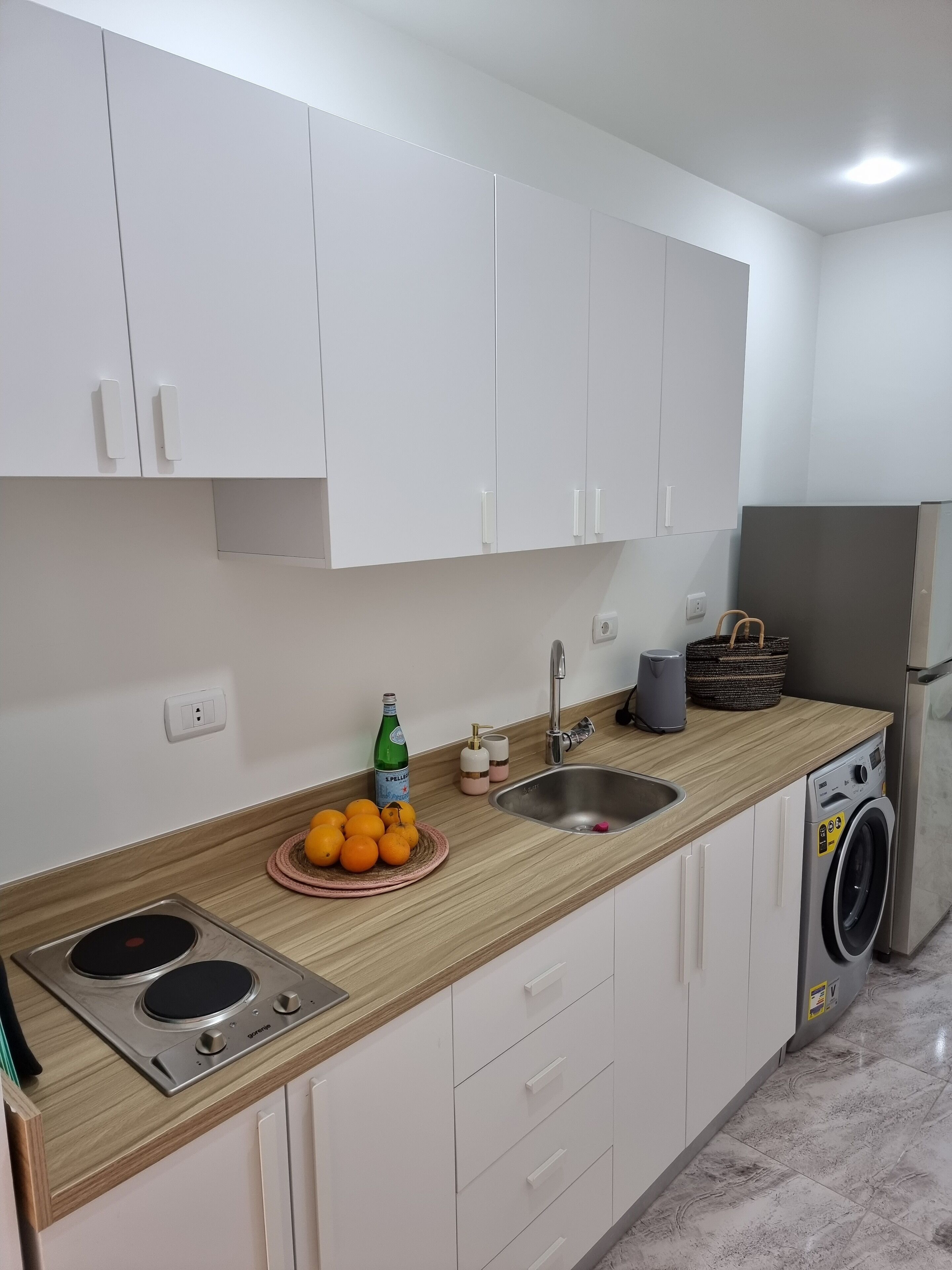 Een moderne keuken met witte kastjes, een roestvrijstalen spoelbak, een ingebouwde wasmachine en een houten aanrecht.