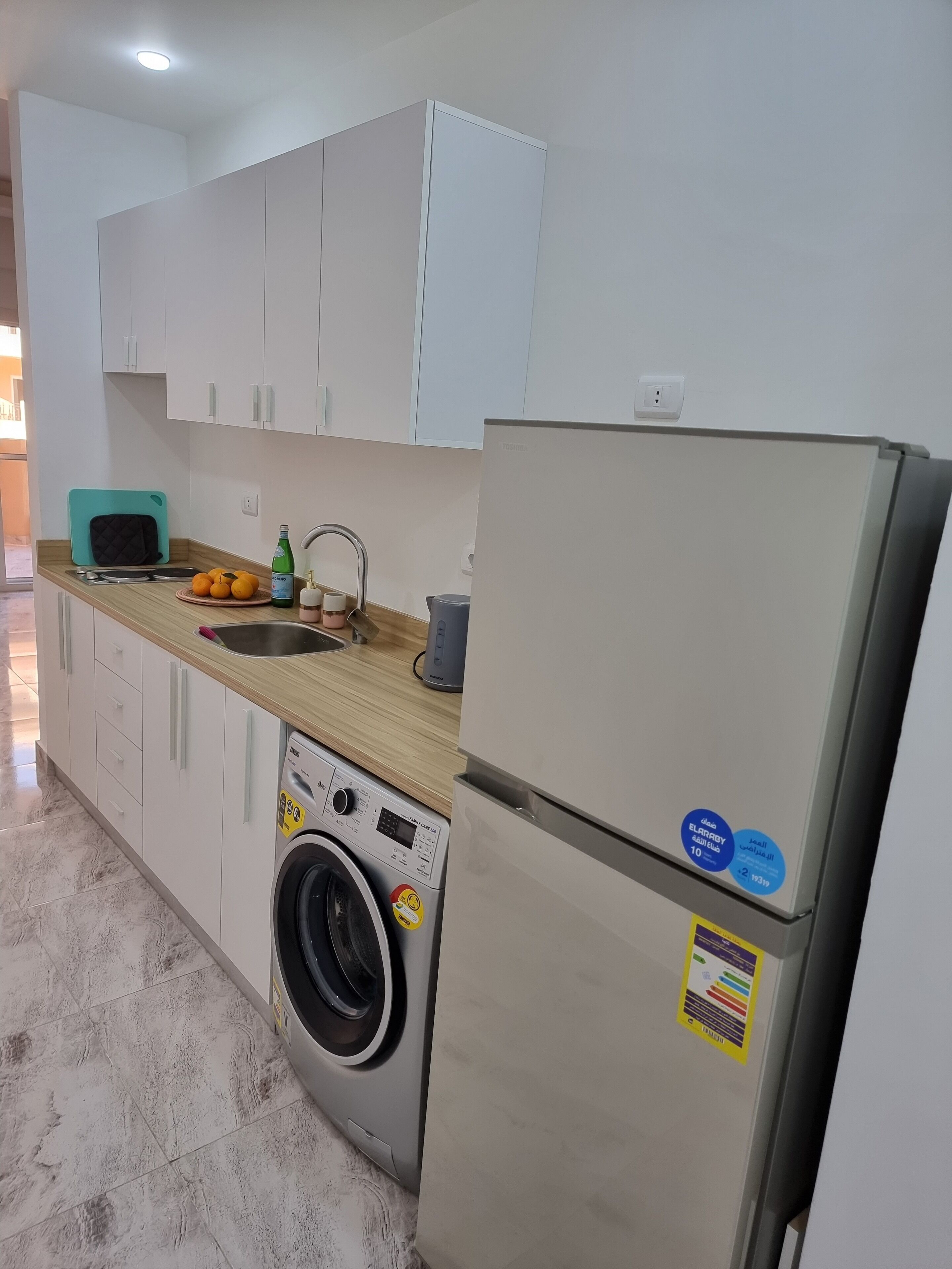 A modern kitchen with white cabinets, a washing machine, a refrigerator, and a sink.