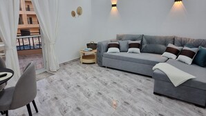 Un salon moderne avec un canapé gris, une petite table d’appoint en bois et un coin repas avec une chaise.